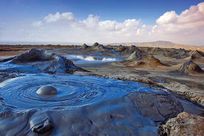 A cluster of active mud volcanoes in Gobustan, Azerbaijan — small grey cones slowly bubbling cold grey mud in a barren, moonlike landscape near Baku to do in Baku Baku travel guide 2026