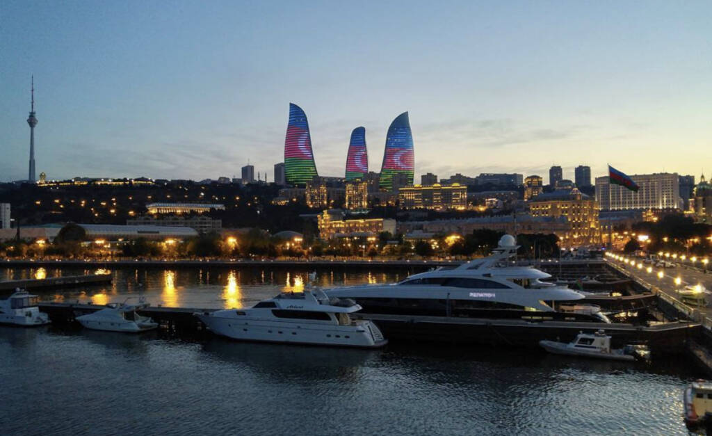 A private luxury yacht sailing on the Caspian Sea at golden hour, with Baku's Flame Towers and illuminated waterfront skyline reflected in the calm dark water to do in Baku Baku travel guide 2026